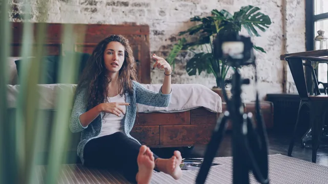 Woman sitting on floor filming vlog, discussing engaging topic. Home setting with cozy atmosphere. Audience and customer separation