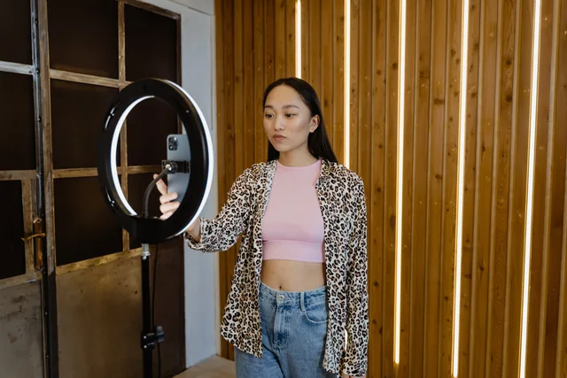 An asian woman influencer filming a vlog with a ring light in a stylish indoor setting. Building a product brand around a creator