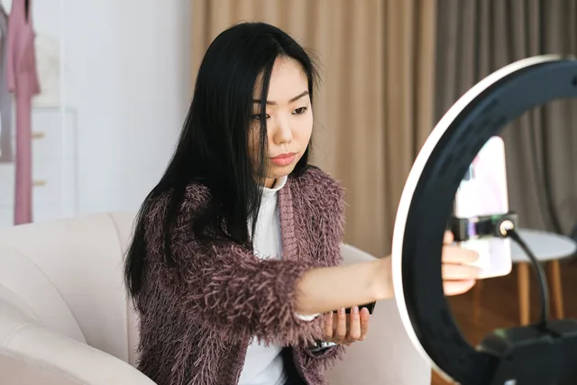 An Asian woman vlogs at home using a smartphone and ring light, perfect setup for influencers. Creator brand reputation risk